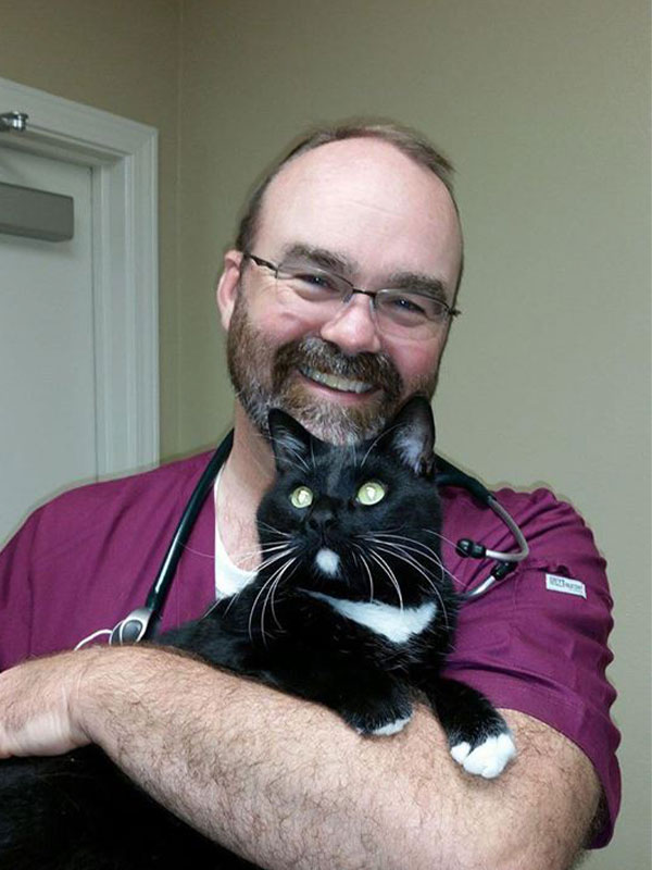 Chris Gentry DVM, veterinarian at Vilonia Animal Clinic in Conway, AR, smiling in red scrubs while holding a black and white cat